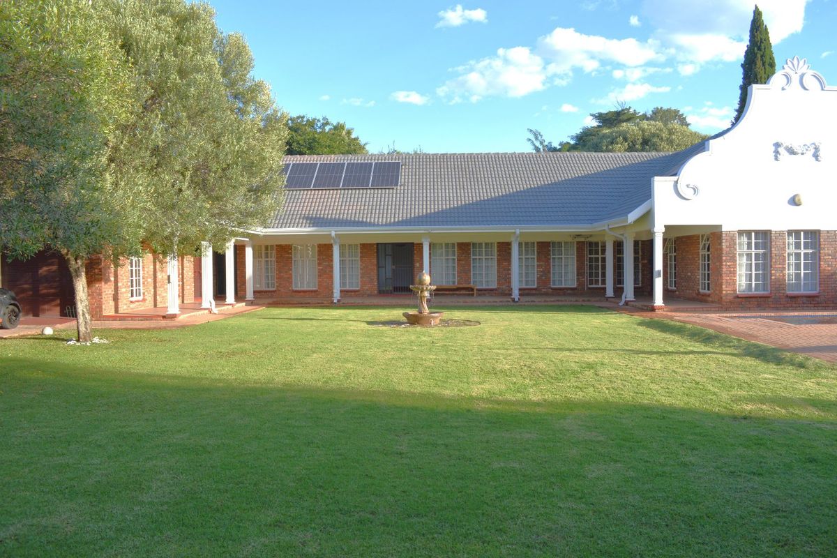 Spacious rear garden featuring a well-maintained lawn, central water fountain, and a covered veranda attached to a brick-built home with solar panels.