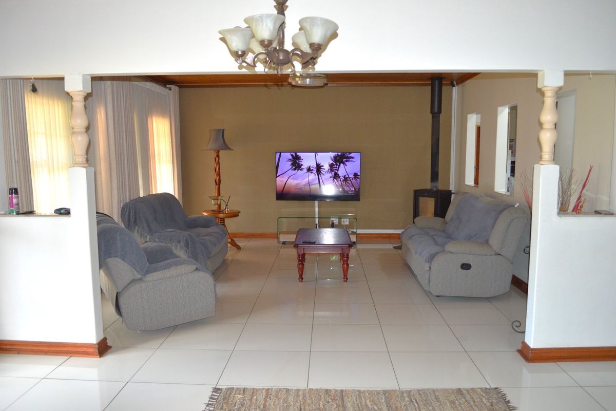 Spacious living room featuring tiled flooring, a freestanding fireplace, and decorative ceiling beams, offering a comfortable and functional layout.