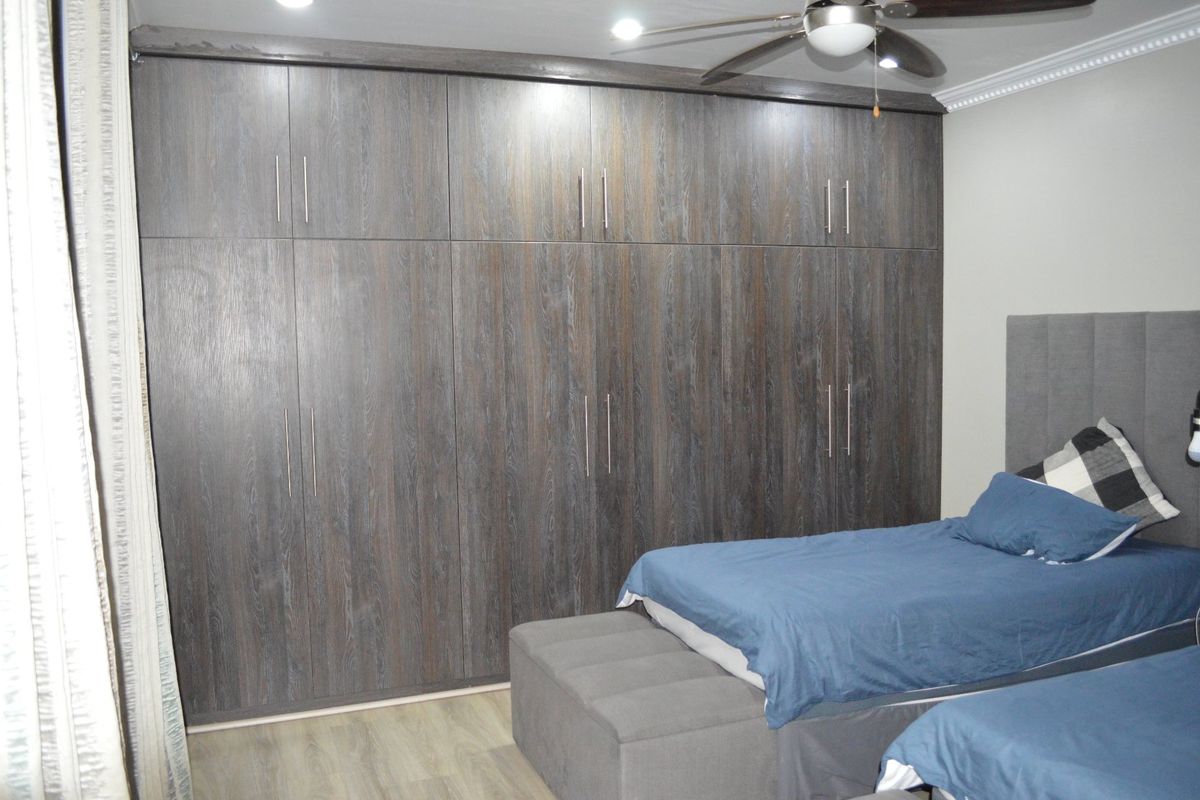 A well-maintained bedroom featuring extensive floor-to-ceiling built-in cupboards, modern laminate flooring, and a ceiling fan.