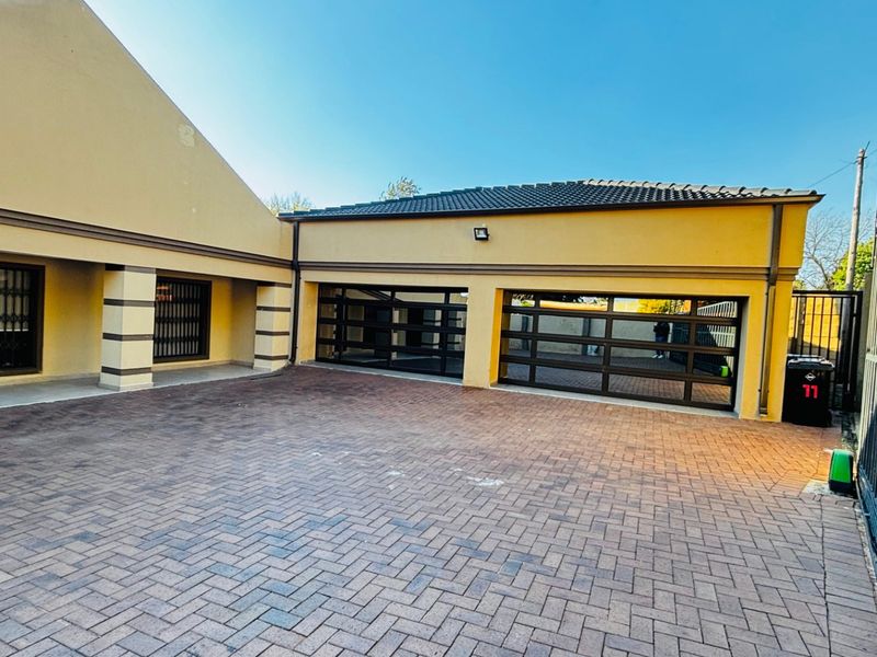 A well-maintained double garage with modern glass-panel doors and a spacious paved driveway, secured by a perimeter gate.