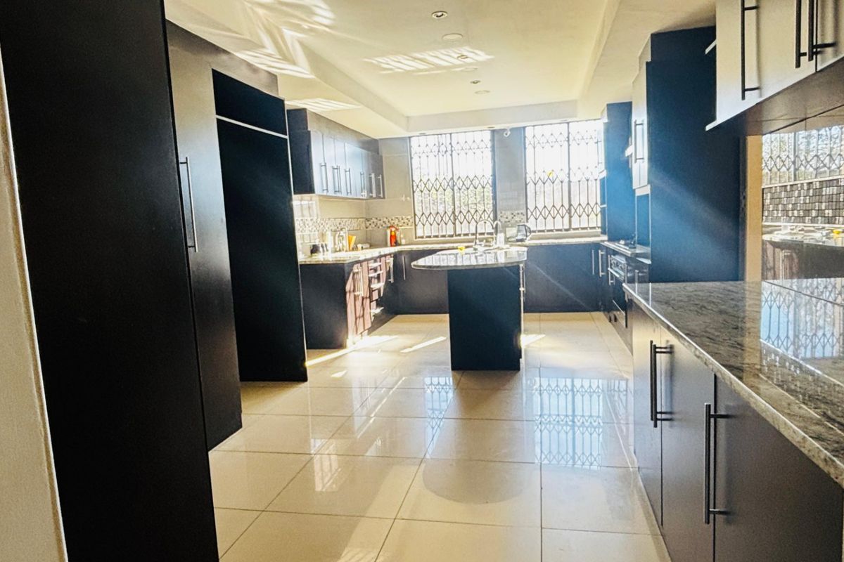 A spacious, modern kitchen featuring dark cabinetry, a central island with granite countertops, tiled flooring, and ample natural light through large windows.