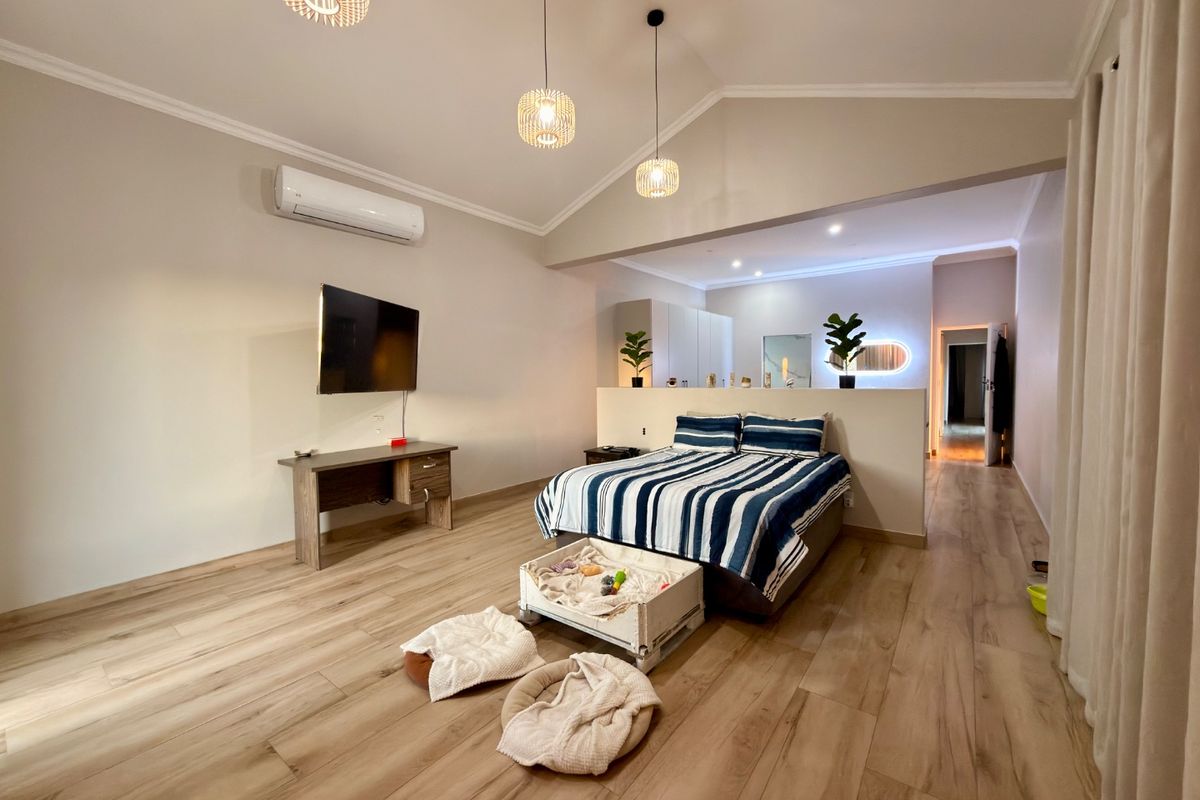 Spacious bedroom featuring vaulted ceilings, laminate wood flooring, split-system air conditioning, and a functional half-wall partition creating a distinct sleeping area.