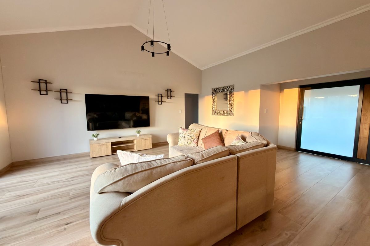 Spacious living room featuring vaulted ceilings, modern laminate flooring, and a large sliding glass door that allows for ample natural light.