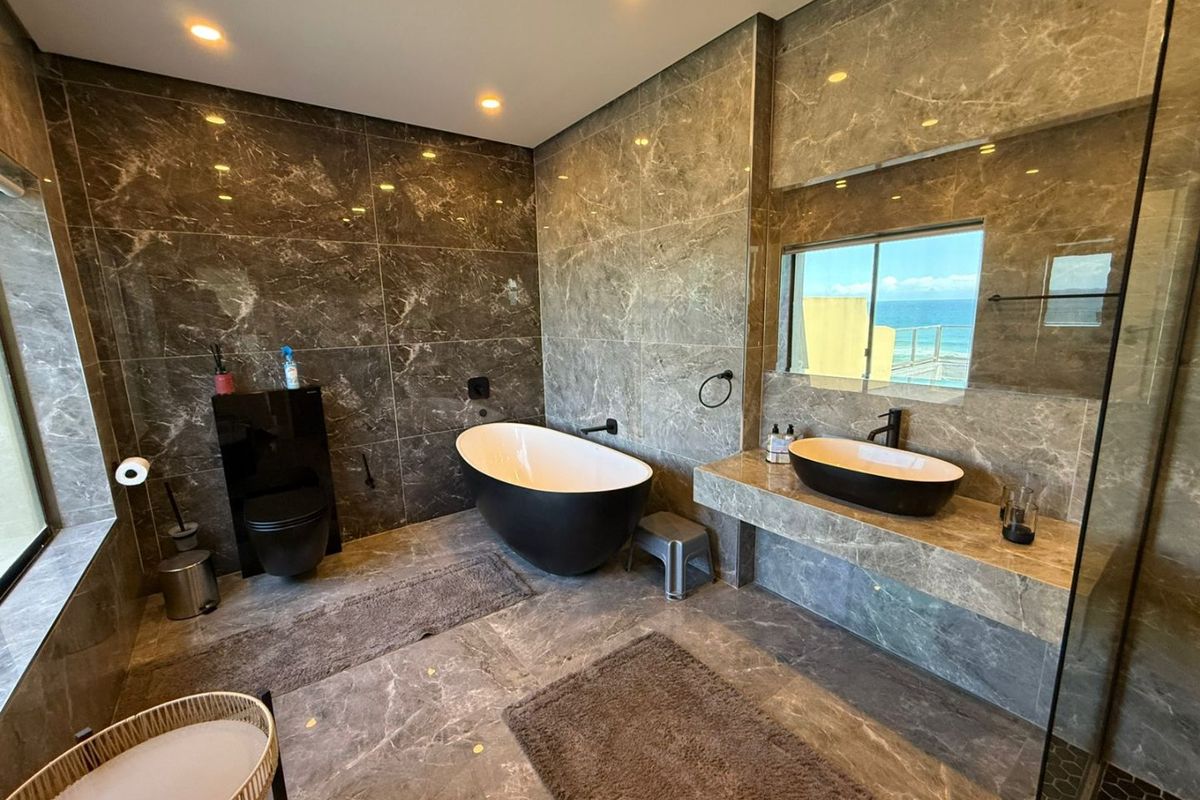 Modern luxury bathroom featuring floor-to-ceiling marble tiling, a sleek freestanding bathtub, wall-mounted toilet, and a stone vanity with a contemporary vessel sink.