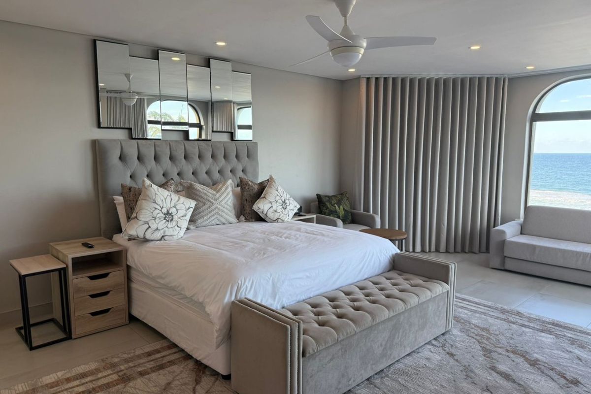 Spacious bedroom featuring neutral tones, recessed lighting, a ceiling fan, and an arched window offering scenic ocean views.