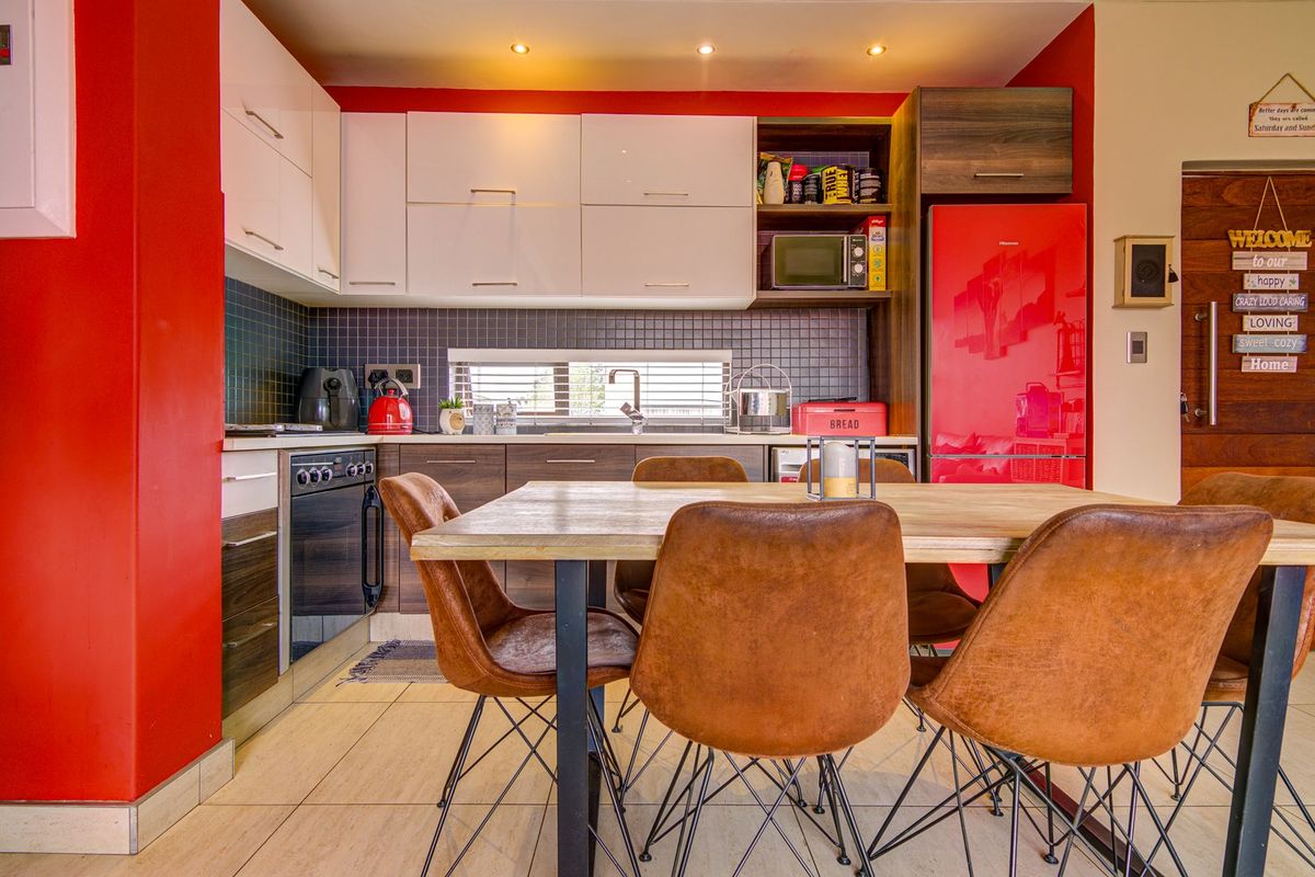 Modern open-plan kitchen featuring high-gloss cabinetry, tiled backsplash, built-in oven, and integrated storage, seamlessly flowing into a dining area with tiled flooring.