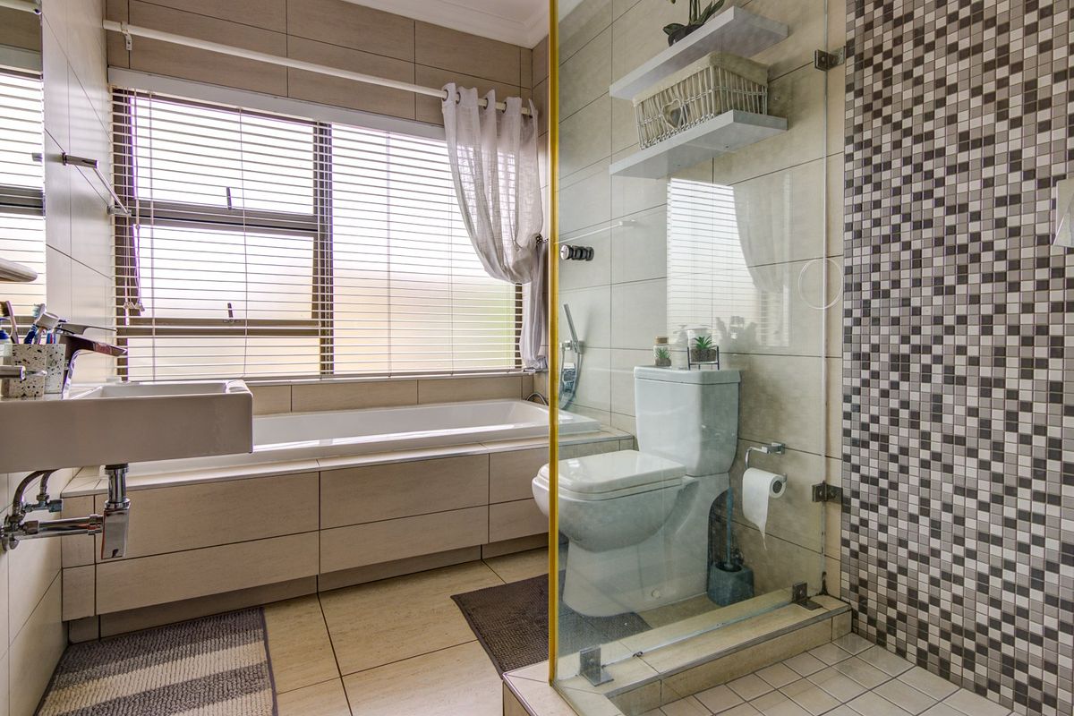 Modern bathroom featuring a built-in bathtub, wall-mounted vanity, and a glass-enclosed shower with decorative mosaic tile accents.