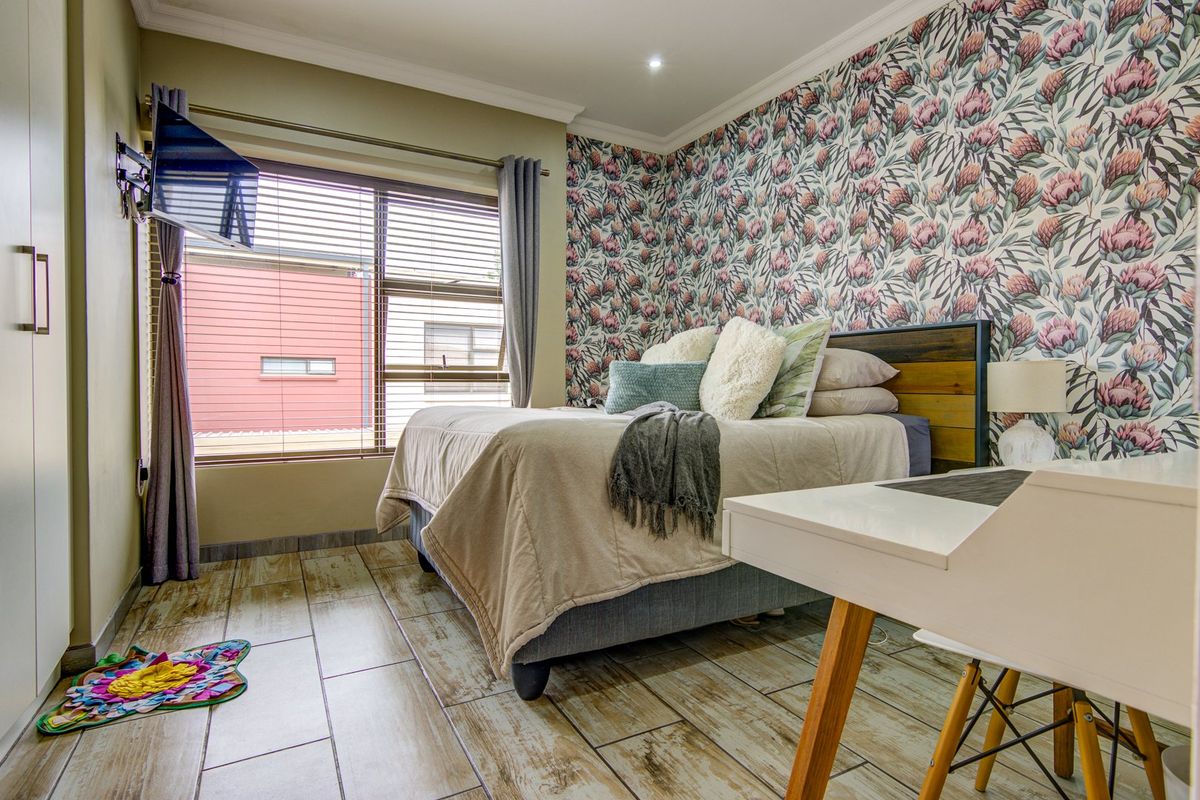 A well-maintained bedroom featuring wood-look tiled flooring, a large window with blinds, and a decorative floral feature wall.