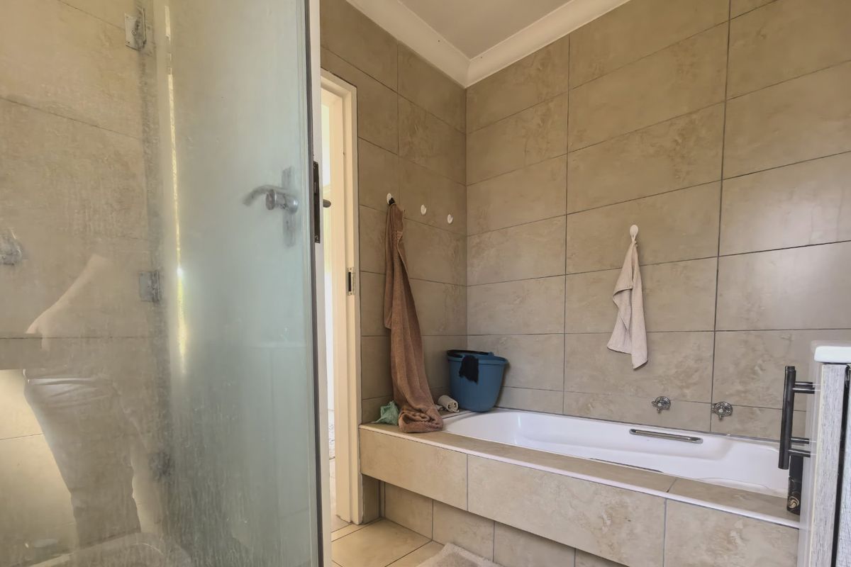 A functional bathroom featuring a built-in bathtub, a separate shower enclosure, and neutral wall tiling throughout.