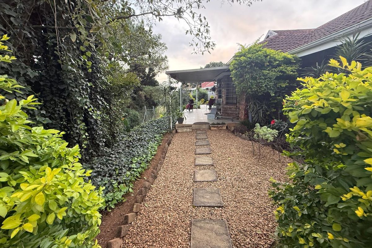 A rear garden pathway featuring gravel surfacing and stone pavers leading to a covered patio area with established landscaping.