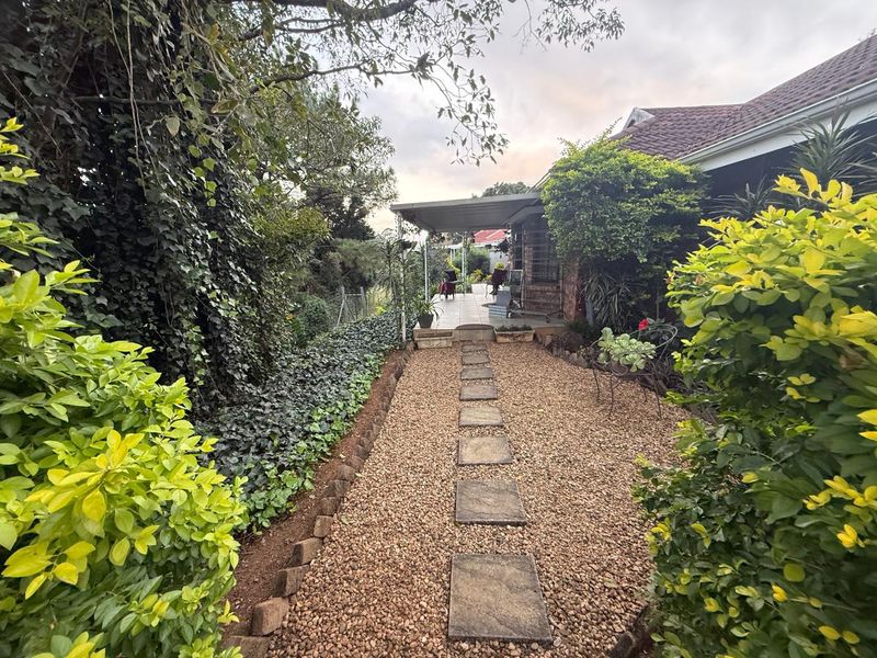 A rear garden pathway featuring gravel surfacing and stone pavers leading to a covered patio area with established landscaping.