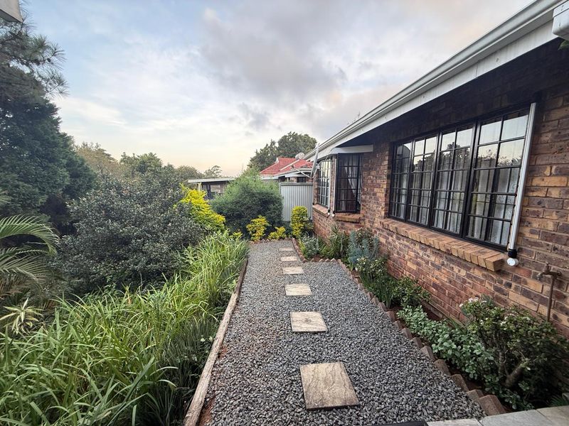 A side garden path featuring gravel surfacing, stone pavers, and established landscaping alongside the brick exterior of the townhouse.