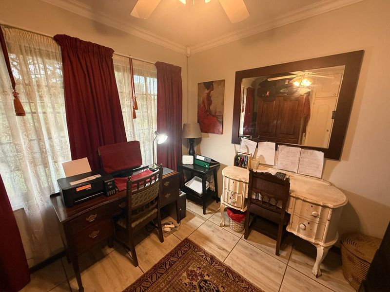 A functional home office space featuring tiled flooring, a ceiling fan, and a large wall-mounted mirror.