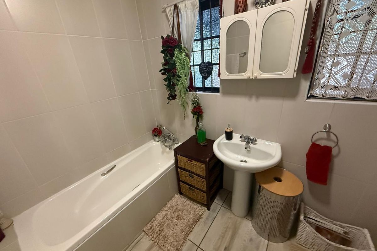 A functional bathroom featuring a white bathtub, pedestal basin, wall-mounted medicine cabinet, and tiled walls and flooring.