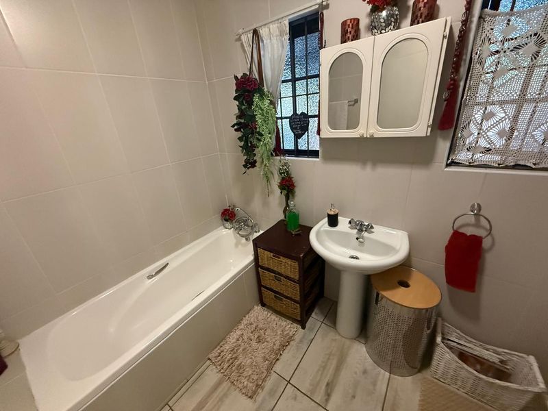 A functional bathroom featuring a white bathtub, pedestal basin, wall-mounted medicine cabinet, and tiled walls and flooring.