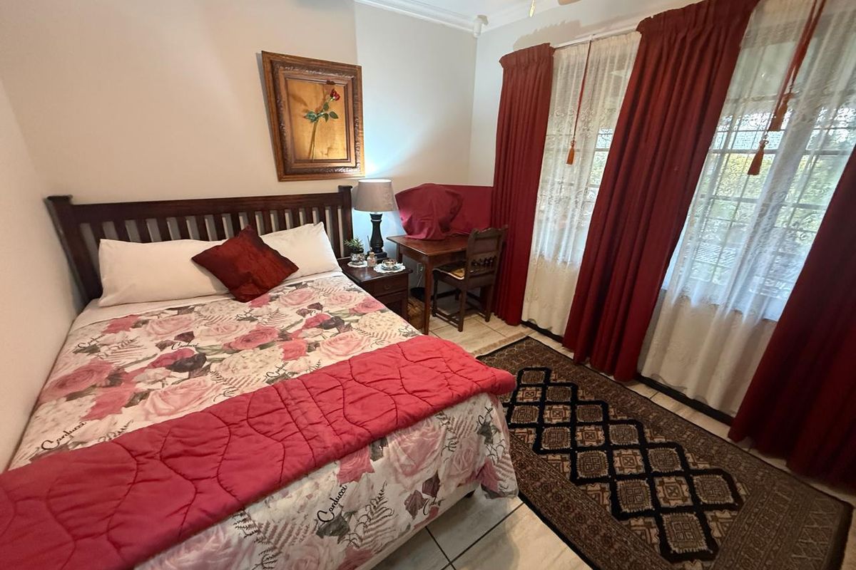 A well-lit bedroom featuring tiled flooring, a ceiling fan, and large windows with curtain treatments.