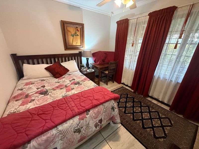 A well-lit bedroom featuring tiled flooring, a ceiling fan, and large windows with curtain treatments.