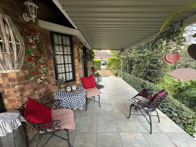 A covered patio area featuring tiled flooring, brick exterior walls, and direct access to the garden, providing a functional outdoor living space.