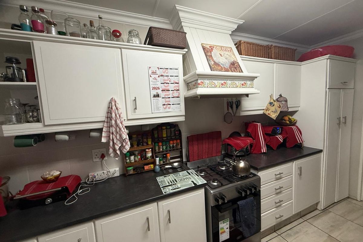 A functional kitchen featuring white cabinetry, dark countertops, a gas stove with an integrated extractor hood, and tiled flooring.