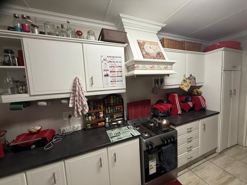 A functional kitchen featuring white cabinetry, dark countertops, a gas stove with an integrated extractor hood, and tiled flooring.