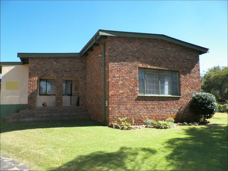 Front view of a face brick house featuring a covered porch with arched detailing, metal window frames, and a well-maintained front lawn.