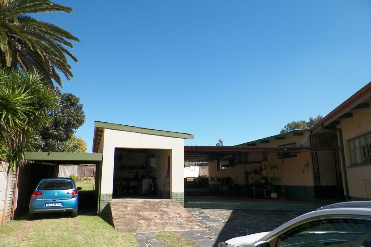 Rear exterior view showing a garage, attached carport, and paved driveway area with a concrete ramp access.