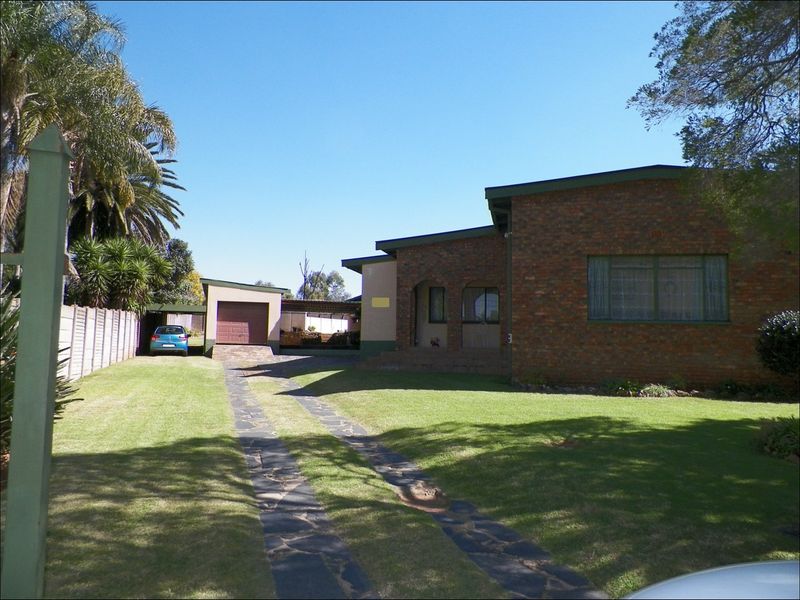 Front view of a face brick house featuring a paved driveway, garage, carport, and a well-maintained lawn.