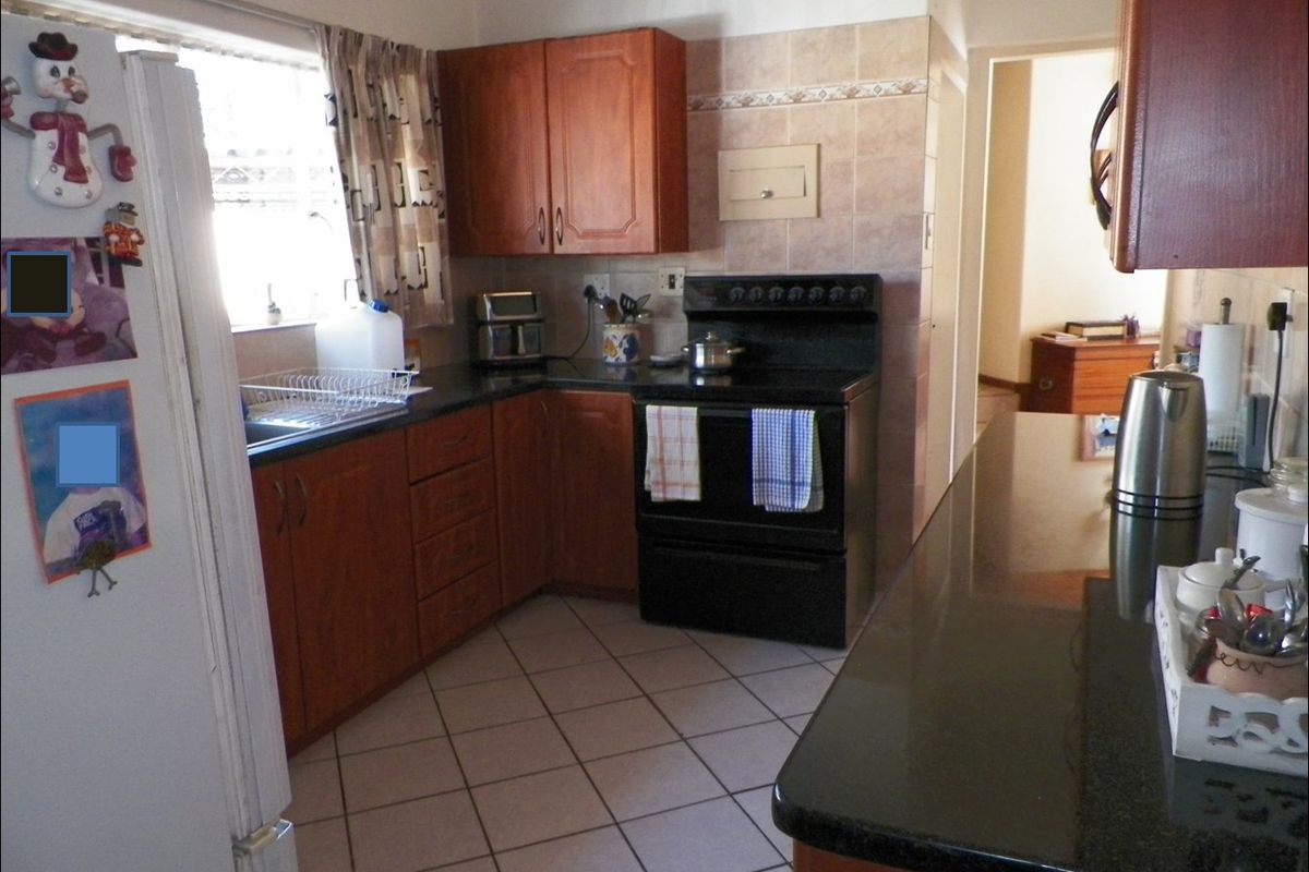 A functional kitchen featuring wooden cabinetry, granite countertops, tiled flooring, and a freestanding stove, offering a practical layout for daily meal preparation.