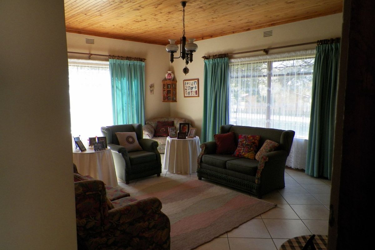 A living room featuring a warm timber tongue and groove ceiling, neutral tiled flooring, and large windows that provide ample natural light.