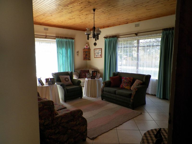 A living room featuring a warm timber tongue and groove ceiling, neutral tiled flooring, and large windows that provide ample natural light.