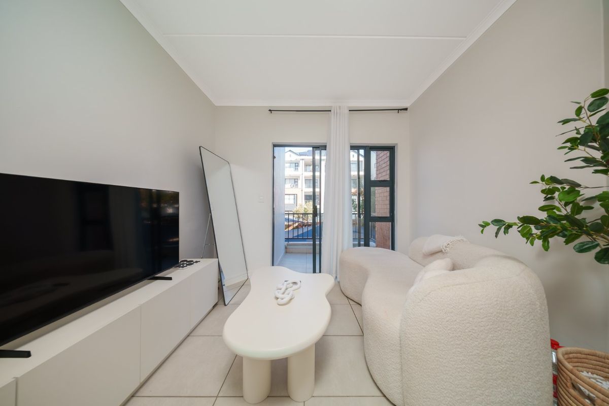 A bright and modern living room featuring neutral tiled flooring, coved ceilings, and a sliding glass door providing access to an outdoor balcony.