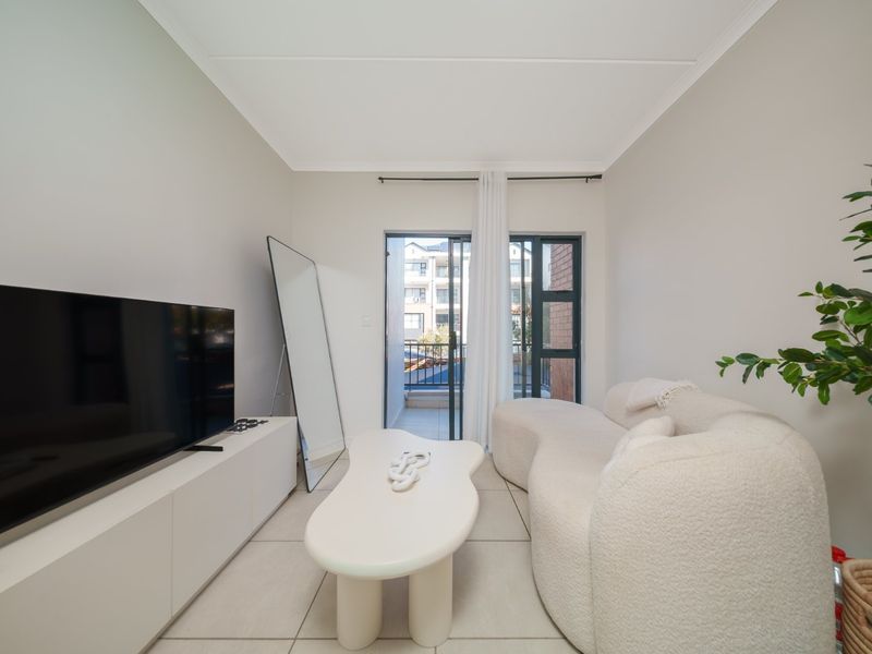 A bright and modern living room featuring neutral tiled flooring, coved ceilings, and a sliding glass door providing access to an outdoor balcony.