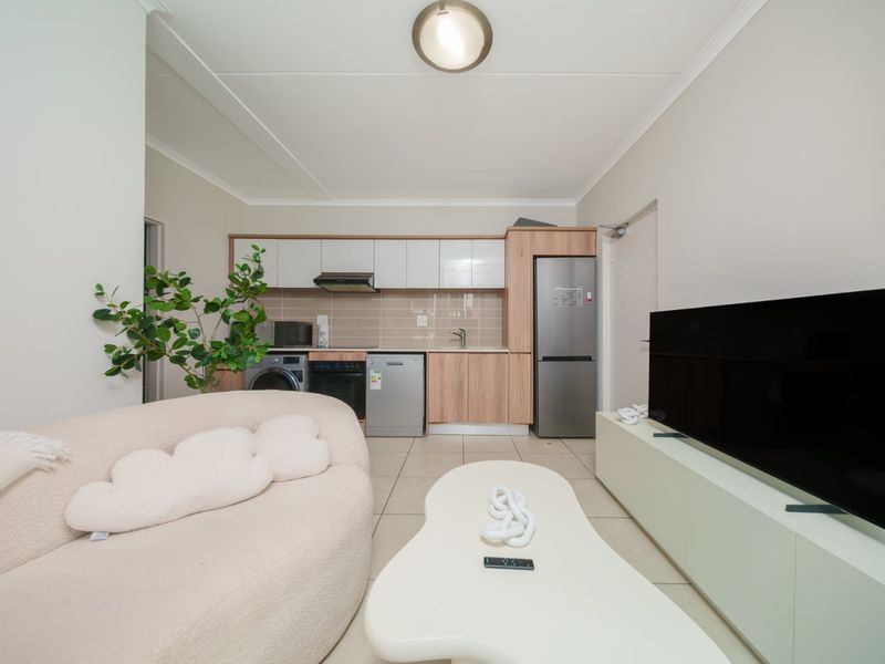An open-plan living area featuring a compact kitchen with modern cabinetry, tiled flooring, and integrated appliances, seamlessly flowing into the living space.