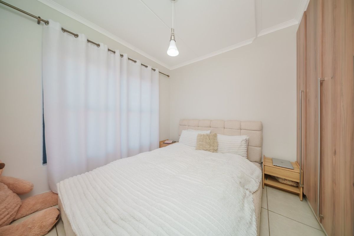 A well-maintained bedroom featuring neutral tiled flooring, built-in wooden wardrobes, and a simple pendant light fixture.