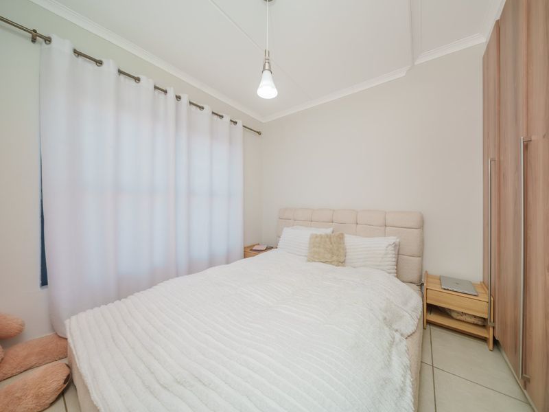 A well-maintained bedroom featuring neutral tiled flooring, built-in wooden wardrobes, and a simple pendant light fixture.