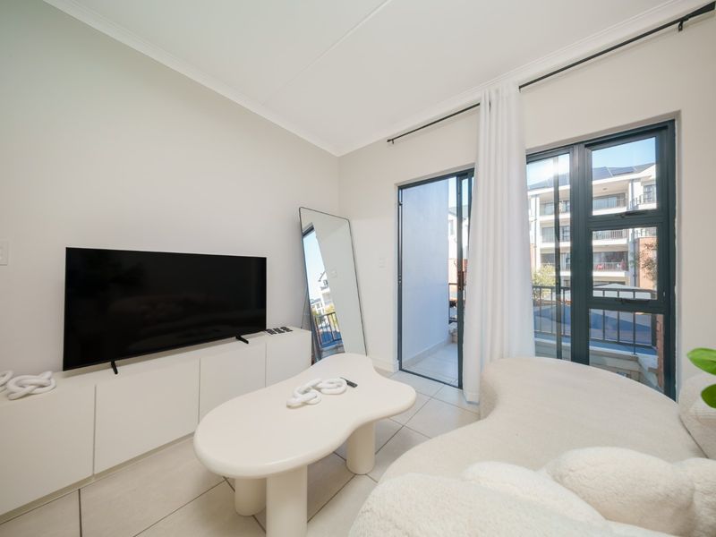 A bright living room featuring tiled flooring and a sliding glass door providing access to a balcony with modern aluminium frames.