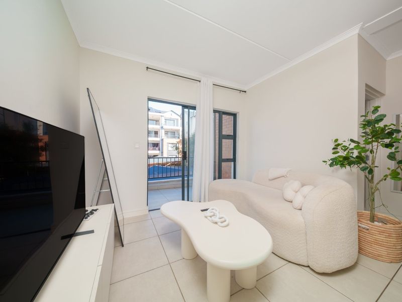 A bright living room featuring tiled flooring and a sliding glass door providing direct access to a private balcony.