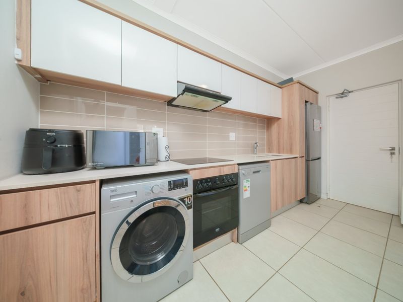 Modern kitchen featuring light wood-grain cabinetry, white upper cabinets, tiled backsplash, and integrated appliances including an oven, hob, and extractor fan.