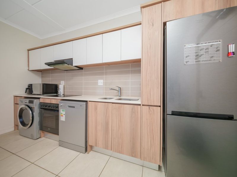 Modern kitchen featuring light wood-grain cabinetry, white upper cabinets, tiled backsplash, and integrated stainless steel appliances including an oven and extractor fan.