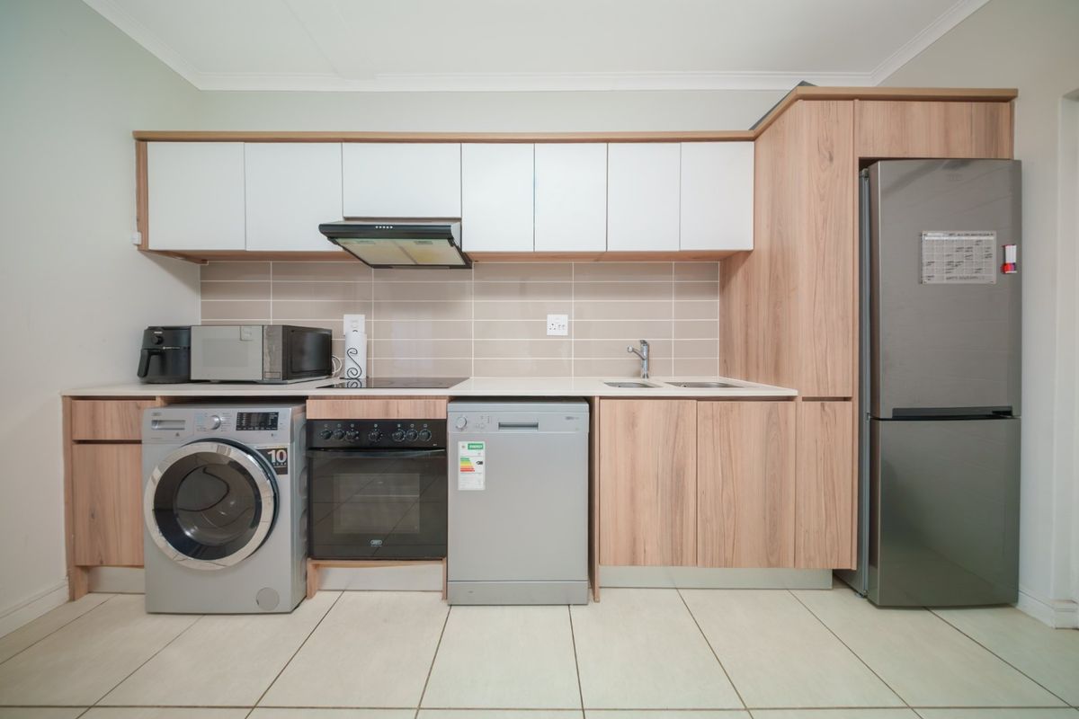 Modern kitchen featuring light wood-grain cabinetry, white upper cabinets, tiled backsplash, integrated appliances, and neutral floor tiles.