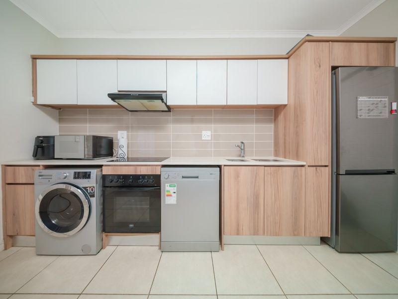 Modern kitchen featuring light wood-grain cabinetry, white upper cabinets, tiled backsplash, integrated appliances, and neutral floor tiles.