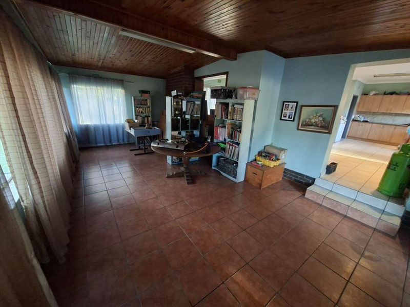 Open plan living area featuring tiled flooring, a timber ceiling, and an exposed brick fireplace, with a raised step leading to the kitchen area.