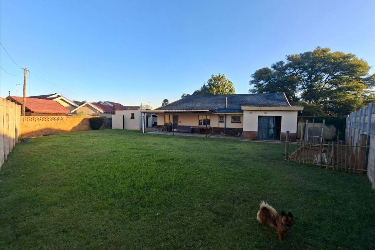 A spacious rear garden featuring a large lawn area, brick boundary walls, and a covered patio attached to the main house structure.