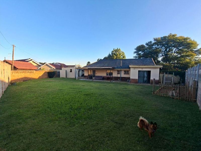 A spacious rear garden featuring a large lawn area, brick boundary walls, and a covered patio attached to the main house structure.