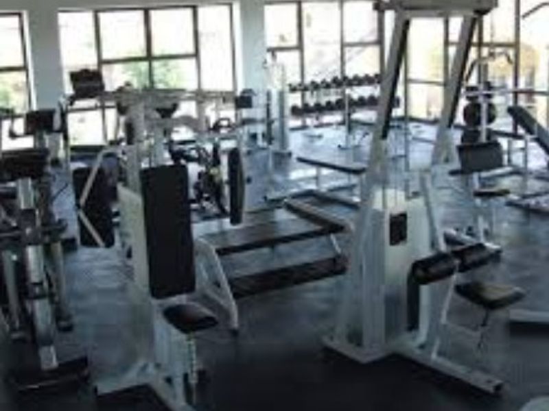 A spacious gym area featuring large windows for natural light, exposed ceiling beams, and durable rubber flooring.