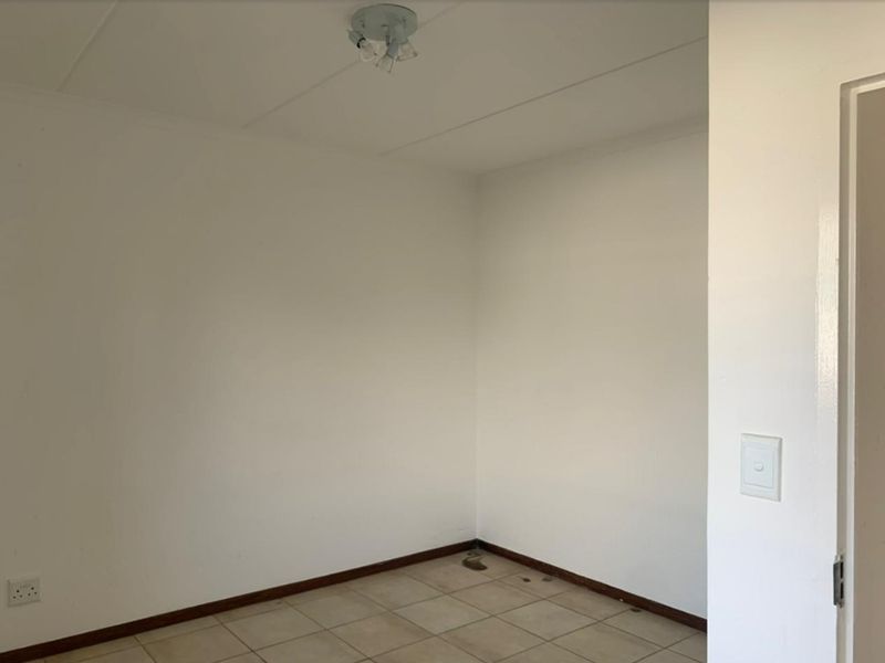 A vacant bedroom featuring neutral tiled flooring, white walls, and a simple ceiling light fixture, offering a blank canvas for personalization.
