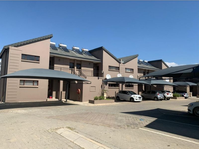 Front elevation of a townhouse complex featuring paved parking areas, shade cloth carports, and roof-mounted solar water heating systems.