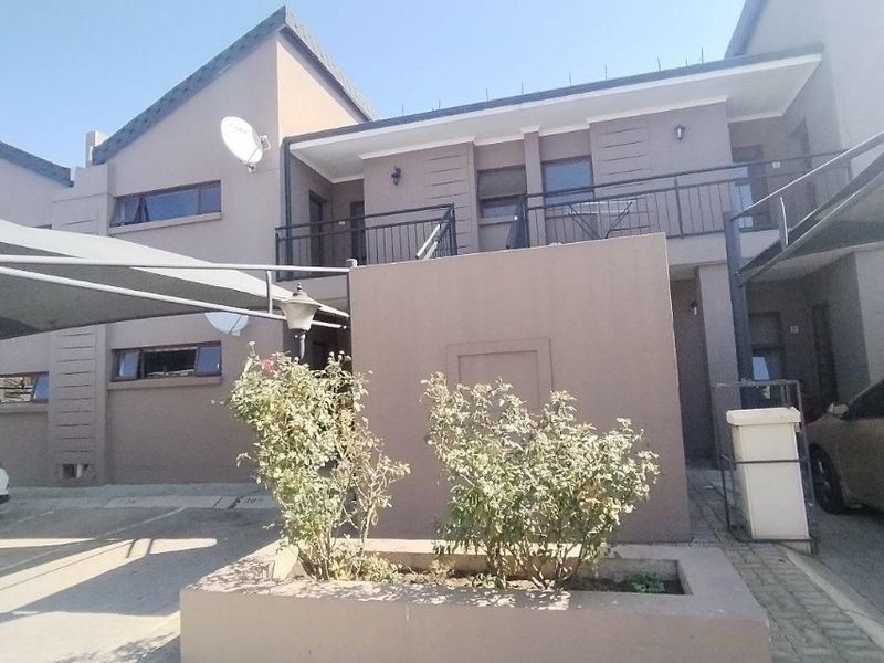 Front elevation of a townhouse featuring a paved driveway, masonry planter box, and an upper-level balcony with metal railings.