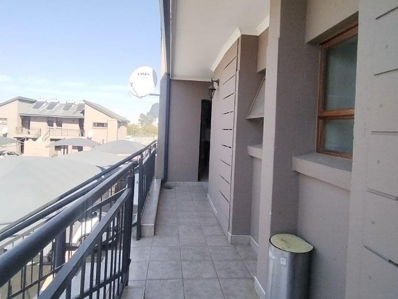 A covered balcony featuring tiled flooring and a metal balustrade, providing an outdoor space with views of the surrounding townhouse complex.