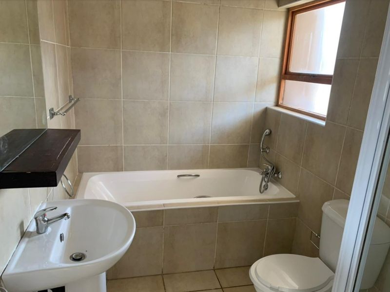 A functional bathroom featuring a built-in bathtub, pedestal washbasin, and toilet, finished with neutral wall and floor tiling.